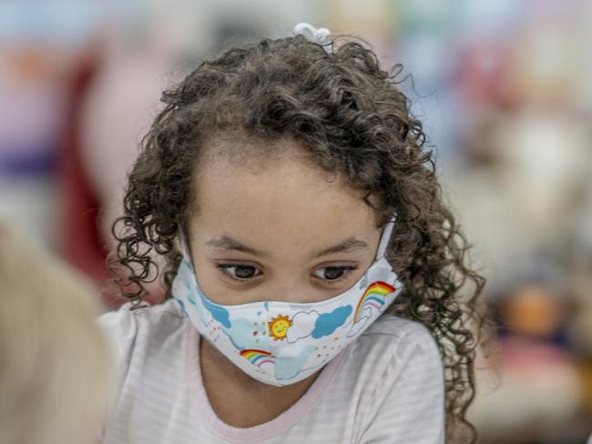 Multi-ethnic group of children colouring at a table while wearing protective face masks to avoid the transfer of germs.