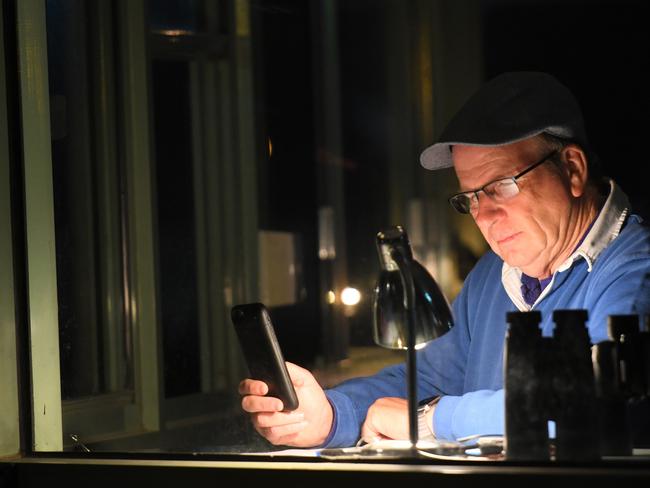 Trainer Robert Smerdon studies his phone at Caulfield trackwork last October. He faces 115 charges relating to the doping scandal. Picture: Vince Caligiuri/Getty