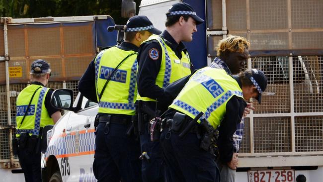 Police officers put a man into the back of a paddy wagon.