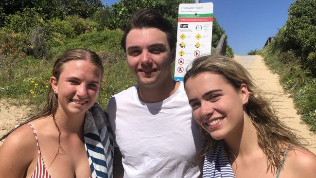 Fran Buffa, 19, of St Ives (left), Harry Davis, 19, of St Ives and Ella Barry, 19, of Freshwater, with a beach hazards sign in the car park at Freshwater Beach. Picture: Jim O'Rourke