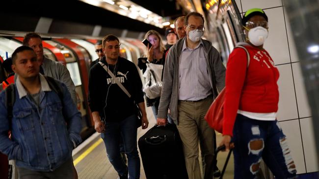 Commuters, some wearing PPE (personal protective equipment) as a precautionary measure against COVID-19, walk along the platform at a tube station in London on April 22. Picture: AFP