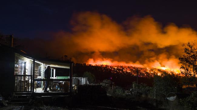 A resident watches from the deck of his shack as firefighters conducting a controlled burn along a ridge line at Miena in the Central Highlands last night. Hot and windy conditions are forecast for today, creating unprecedented fire risk conditions. Picture: HEATH HOLDEN