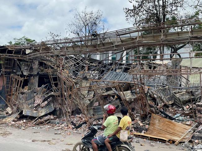 This photo taken on August 10, 2024 shows motorists riding past a burnt-out building in Lashio in Myanmar's northern Shan State, following fighting between Myanmar's military and Myanmar National Democratic Alliance Army (MNDAA) in the region. (Photo by AFP)