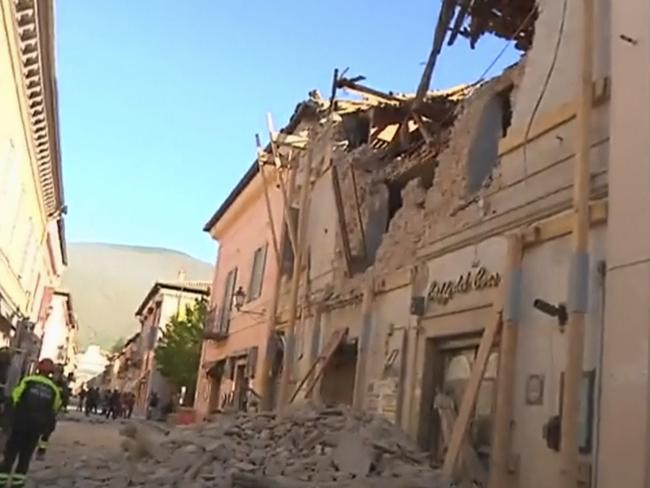 Firefighters stand in front of a damaged building in Norcia. Picture: Sky Italia via AP