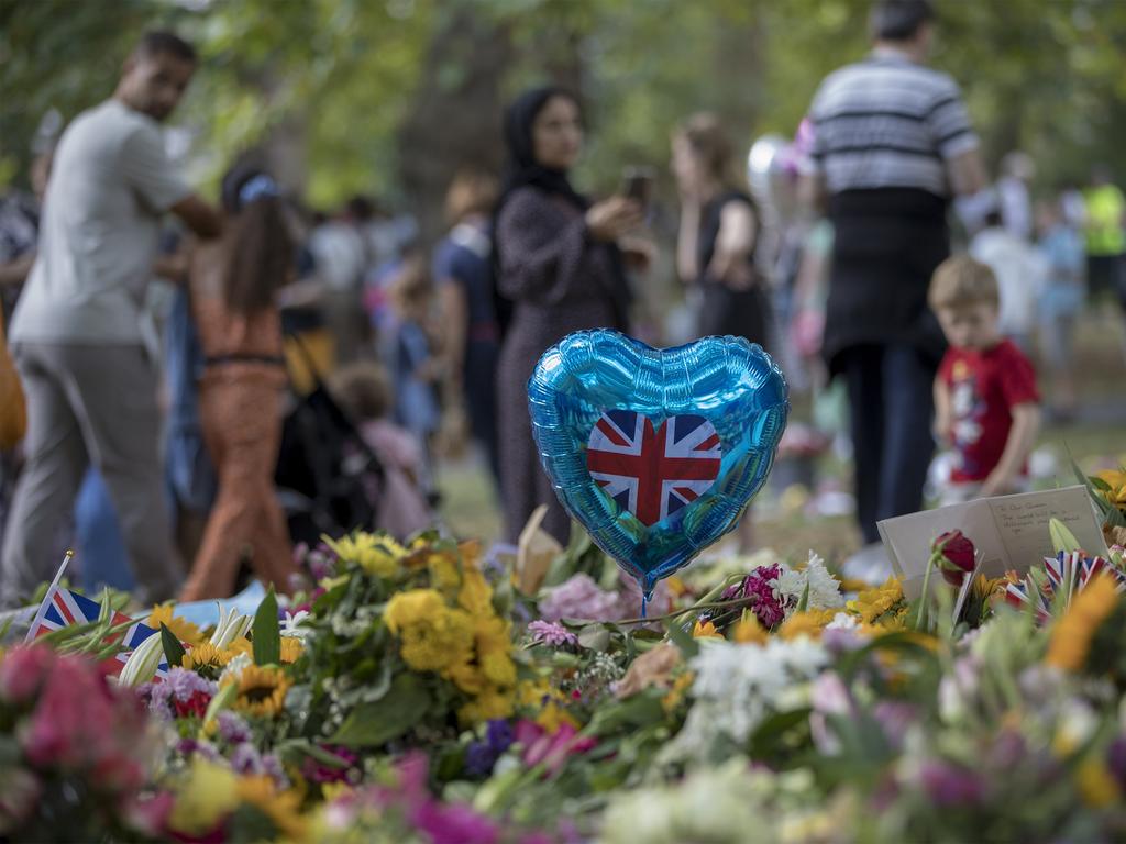 Members of the public walk through flowers, balloons and tributes left by mourners outside Buckingham Palace that have been moved to Green Park. Picture: Ella Pellegrini