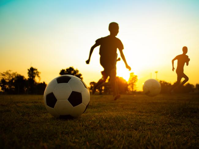 Silhouette action sport outdoors of a group of kids having fun playing soccer football on green grass field