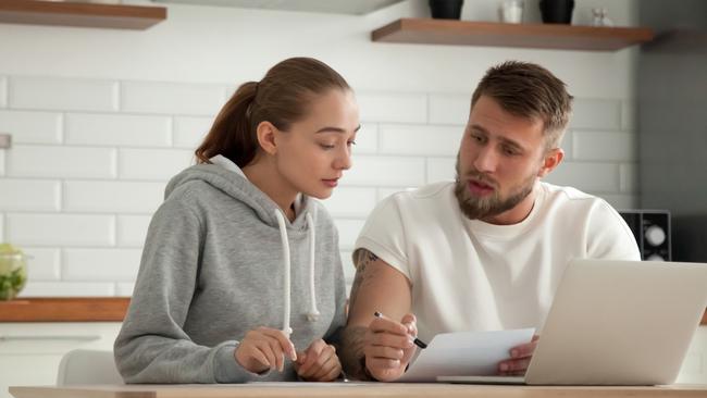 Focused young couple checking analyzing utilities bills sitting together at kitchen table, serious husband and wife reading bank loan documents with laptop, family managing finances planning expenses; money generic