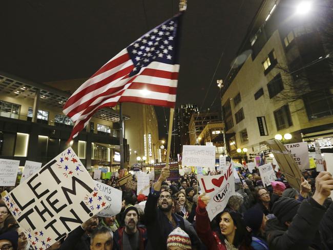 A protester waves a US flag as another holds a sign that reads "Let Them In" during a march and rally to oppose President Donald Trump's executive order in Seattle. Picture: AP