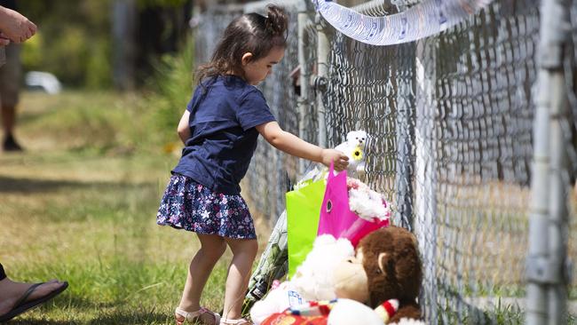 A little girl adds to a growing collection of flowers and soft toys left near where two little girls died south of Brisbane yesterday. Picture: Attila Csaszar/AAP