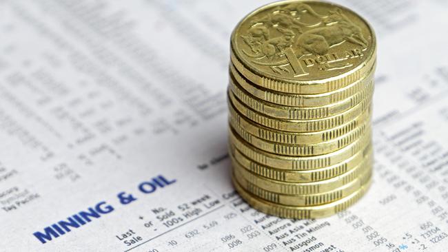 Eleven Australian one dollar coins stacked on a newspaper reporting share market prices for Mining and Oil. generic investing