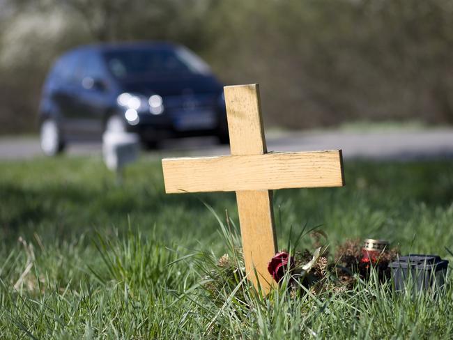 A wooden roadside memorial. In the background an unrecognisable car drives by the scenery. Selective focus