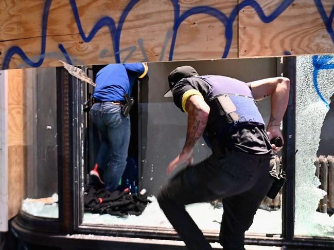 Police officers jump through a broken store window in New York City. Picture: AFP