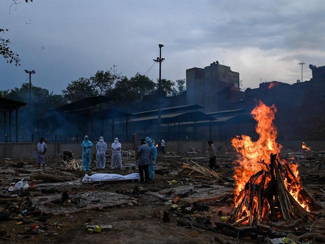 Relatives in personal protective equipment suits stand near the body of a person who died due to the COVID-19, at a cremation ground in New Delhi. Picture: AFP