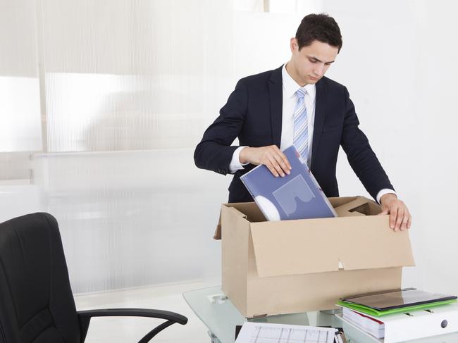 Sad young businessman packing files in cardboard box at desk in office