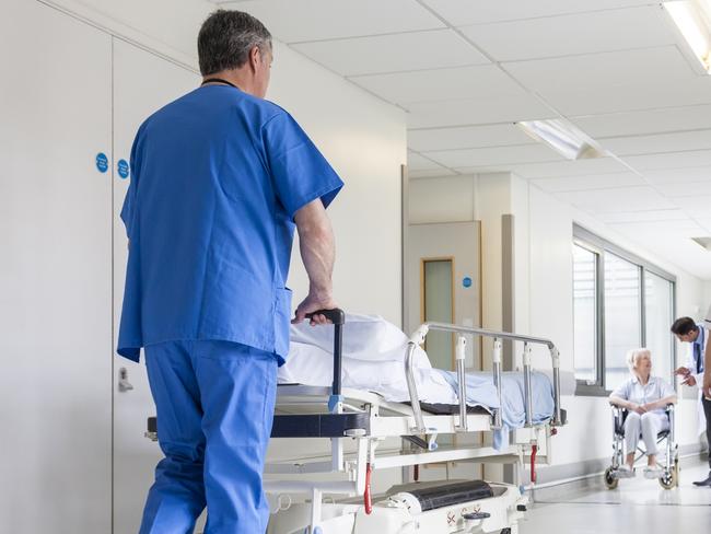 Male nurse pushing stretcher gurney bed in hospital corridor with doctors & senior female patient