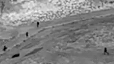 An officer and his police dog (far left shadow) keep an eye on two suspects laying on the ground (long shadow second from left) from the other side of a fence as three other police officers descend on their position. Still image: NT Police drone footage