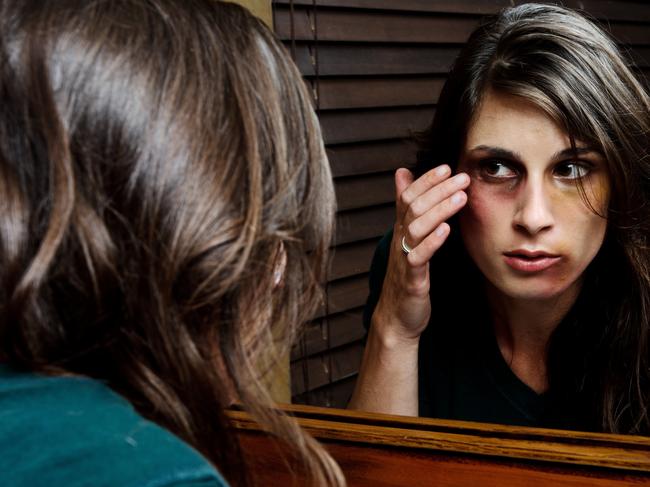 Battered woman checks the extent of her injuries in the bathroom mirror