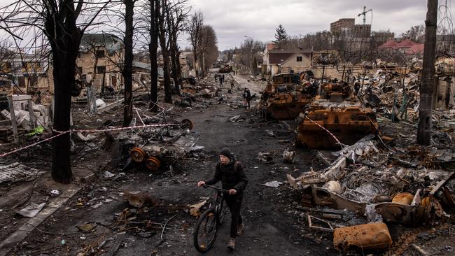 A man pushes his bike through debris and destroyed Russian military vehicles on a street on April 6 in Bucha, Ukraine.