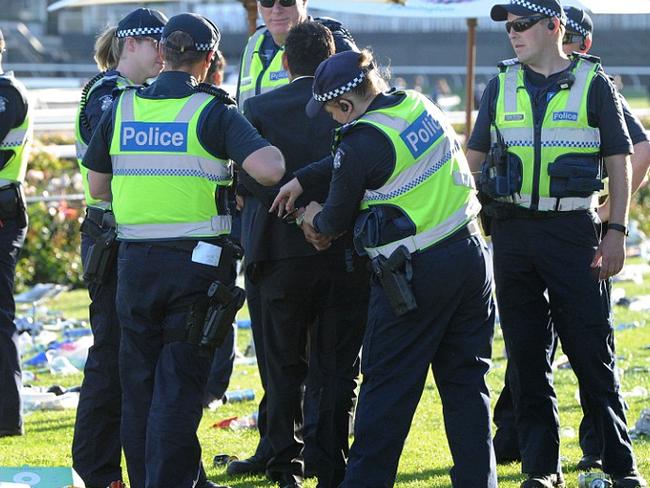 A man is handcuffed by police in the litter strewn field at Flemington after a sunny day of punting and drinking. Picture: AAP.