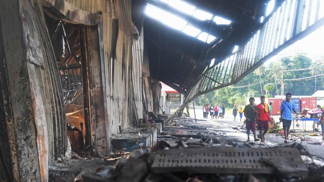 Manus locals walk past the island’s burned out supermarket. Picture: Brian Cassey