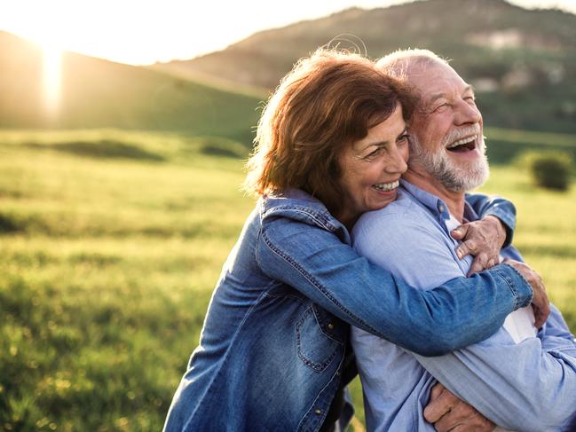 Happy senior couple outside in spring nature, hugging at sunset. Side view.