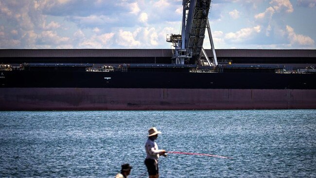 Fishermen stand on a pier in front of a bulk carrier being loaded at the Port of Newcastle in Newcastle.