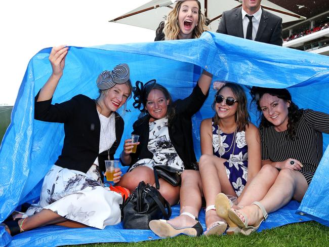 2014 AAMI Victoria Derby Day, Flemington, Victoria. Tessa Cake, Jess Orchard, Lyn Patterson and Nicole Mowthorpe hide from the showers. Picture: Mark Stewart