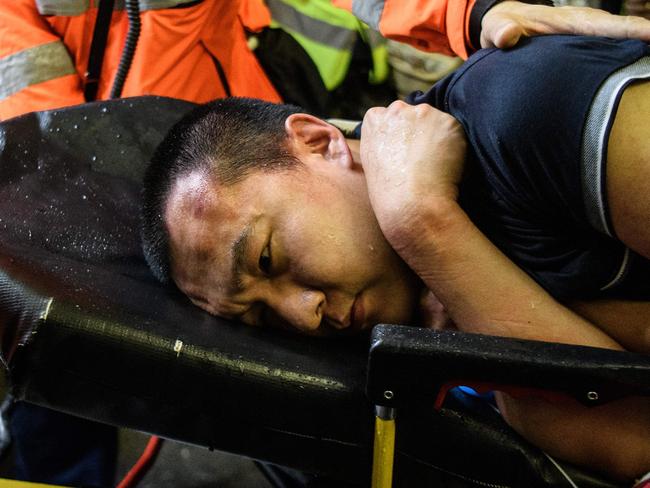 An injured man who was suspected by protesters of being a Chinese spy is taken away by paramedics. Picture: AFP