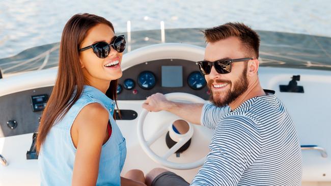 Cheerful young couple looking at camera and smiling while driving yacht. Boating generic.