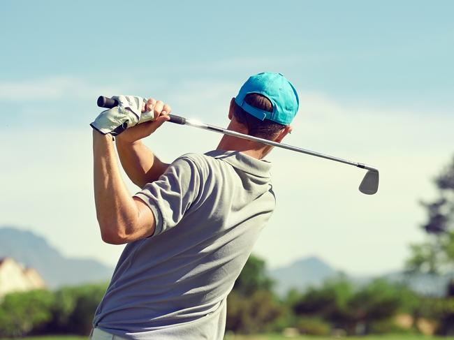 Golfer hitting golf shot with club on course while on summer vacation