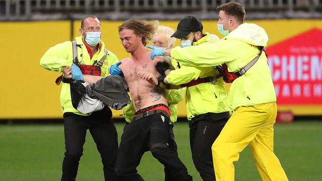 The pitch invader is escorted from the field of play by security during the round 7 AFL match between the Geelong Cats and the Collingwood Magpies at Optus Stadium. Picture: Getty Images.