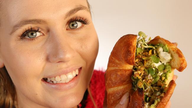 Local &amp; Co staff member Emma Stewart tucks into a crushed avo croissant at the Main Beach cafe. Picture Glenn Hampson