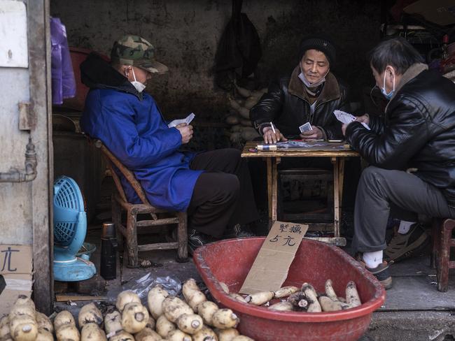 Vendors play cards while wearing protective masks in an alley in Wuhan. Picture: Getty