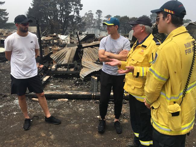 Test cricketers Tim Paine and Nathan Lyon on the fire ground with Ku-ring-gai Brigade deputy captain John Corry and RFS volunteers at Wingello. Pictures: RFS