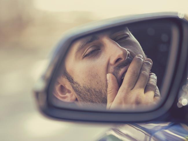 Side mirror view reflection sleepy tired fatigued yawning exhausted young man driving his car in traffic after long hour drive. Transportation sleep deprivation accident concept