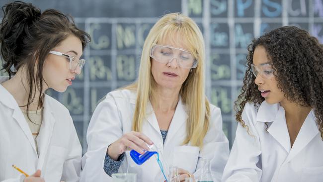 A multi-ethnic group of high school students are working in a science class together. They are mixing solutions and solvents in beakers.