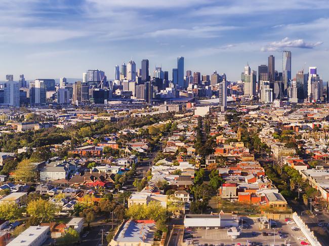 Aerial view of Melbourne city CBD high-rise towers from Port Melbourne and Southbank above residential suburb house roofs and local streets, roads, cars and parks.