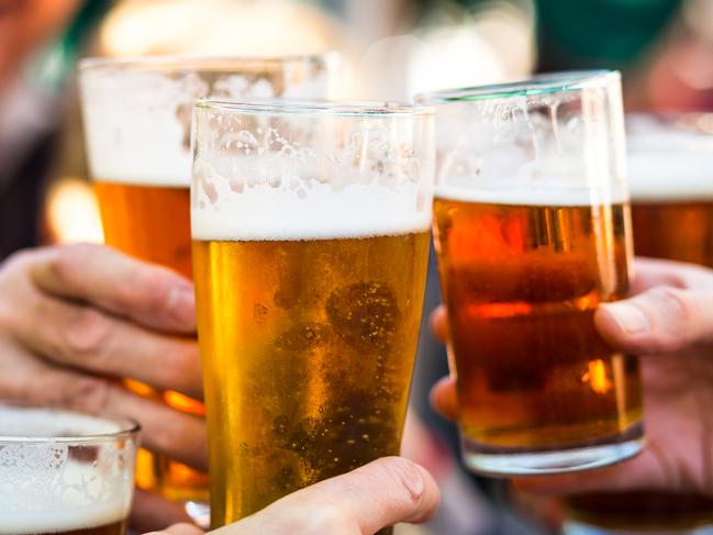 Close up color image depicting a group of people celebrating with a toast. The people cheers their glasses of beer (pints of beer) together in a gesture of celebration, togetherness and happiness. The people are defocused in the background, while focus is on the glasses of beer in the foreground. Room for copy space.