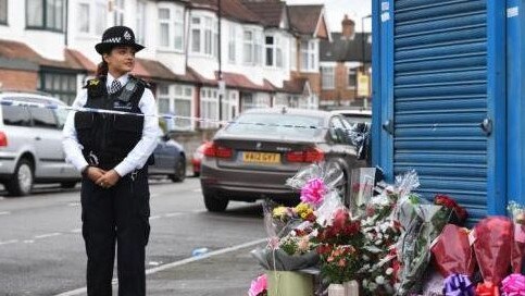 A police woman stands over flowers left for a murder victim.