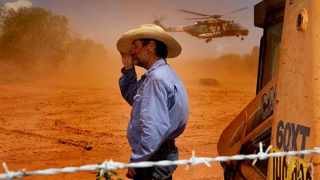 Jack Andrews, Station Manager at Yeeda Station, shelters from the dust as an Australian Army MRH-90 Taipan delivers animal feed to Yeeda Station that has been cut off during recent flooding as part of Operation Flood Assist 23-1. Picture: LACW Kate Czerny