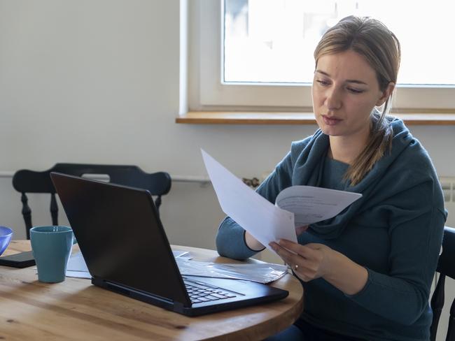 Young woman sitting in the kitchen and calculate household expenditures.