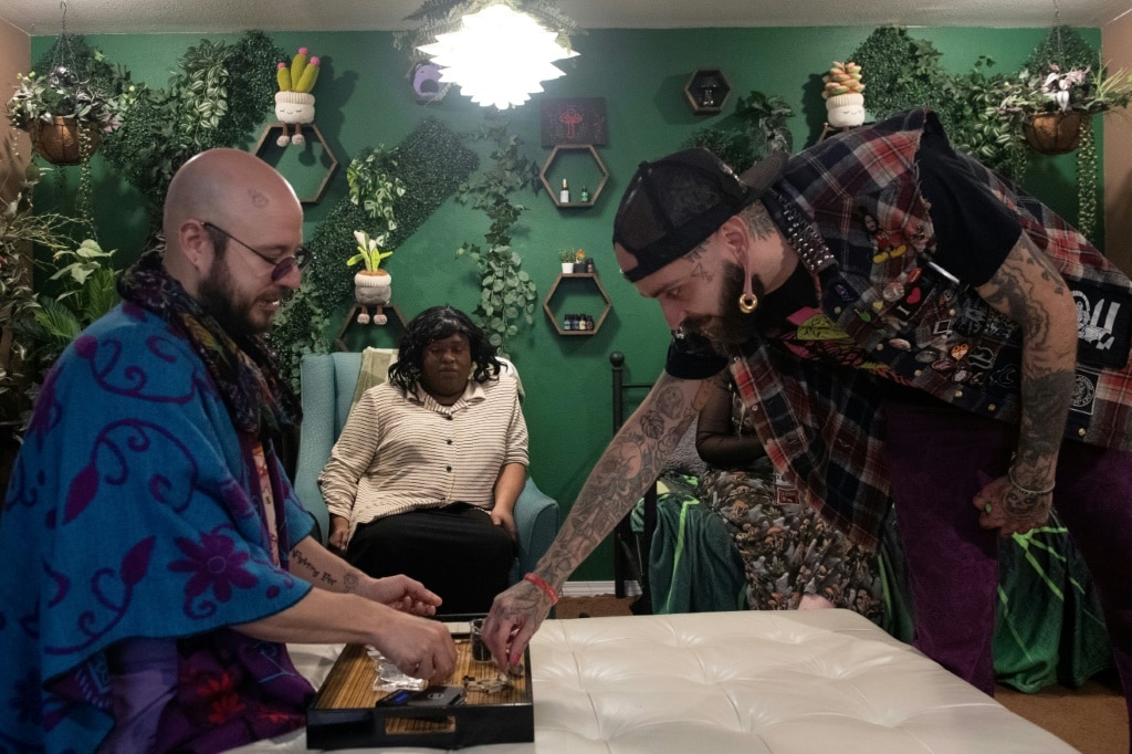 Surrounded by plastic plants and wearing circular blue sunglasses, Benji Dezaval distributes 'magic mushrooms' during group and individual sessions that he supervises