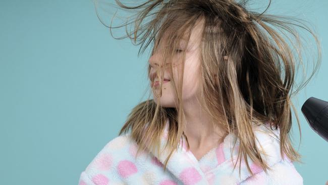 Generic image of young girl drying her blonde hair with electric hairdryer.