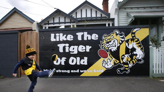 Luca Gilchrist, 3, kicks a footy next to their brick fence with a Tigers mural. Picture: David Caird