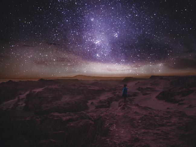 ESCAPE: Woman enjoying stargazing under the night sky with million of stars and Milky Way at beautiful canyon on Atacama Desert in Chile. Picture: Istock