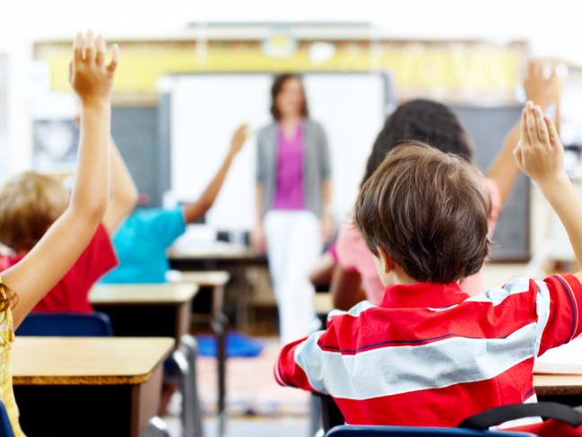 Rear-view of students raising their hands to answer the teacher's question