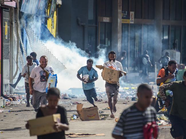 Crowds leave shops with looted goods in Port Moresby. Picture: AFP