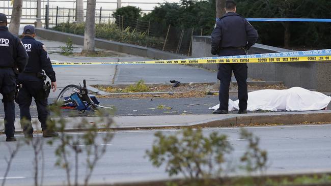 A New York Police Department officer stands next to a body covered under a white sheet near a mangled bike along the bike path.