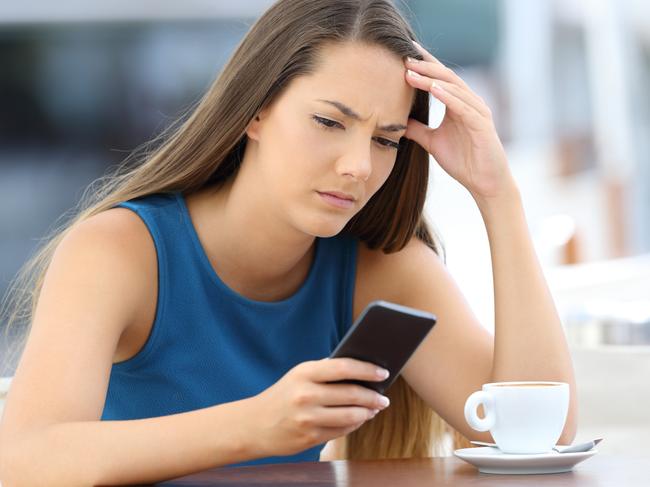 Single worried woman watching a mobile phone and waiting for a call or message sitting in a coffee shop