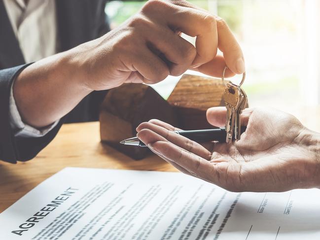 Estate agent giving house keys to customer and sign agreement in office.